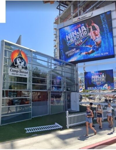 A group of people walk past a large billboard in front of a building.